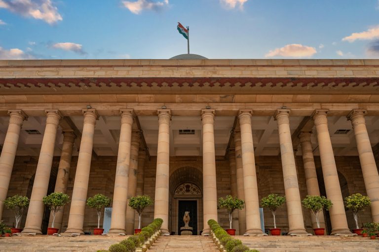 Government building in New Delhi featuring columns and an Indian flag under a vibrant sky.