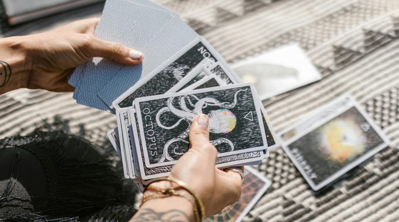Hands holding tarot cards during a reading session on a patterned mat.